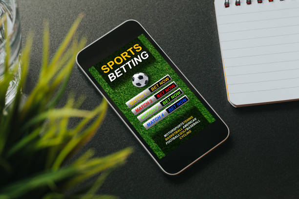 Sports betting website in a mobile phone screen placed over a black desk.